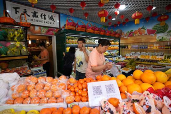 5月8日,店主王继高(前左)在三源里市场精品水果厅内接听客户电话。