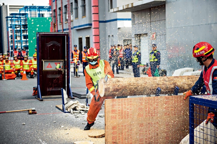2021年10月13日，北京市首届消防行业职业技能竞赛在北京市消防救援总队训保支队拉开帷幕。图为在应急救援员项目的综合破拆模块中，选手正在用油锯切割圆木障碍以营救“被困人员”